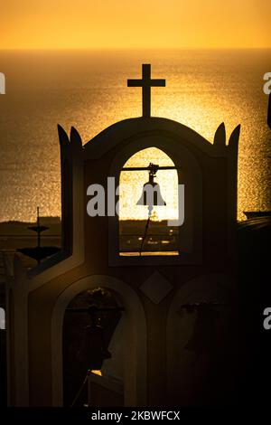 Alba su una chiesa con la sagoma della cupola, croce, campana e uccelli. La piccola cappella come si vede con il sole che riflette dal mare la mattina presto a Santorini Volcano Island nelle Cicladi, Mar Egeo in Grecia il 6 luglio 2020. Le autorità greche hanno revocato le misure di blocco del Coronavirus Covid-19 e hanno permesso la prima ondata di turisti al 15 giugno e poi dal luglio 1 con voli diretti verso le isole, ma verso paesi specifici con casi di pandemia bassa. L'industria del turismo è una delle principali fonti di reddito per il paese, quindi la Grecia ha iniziato ad allentare le misure cercando di tenere il passo Foto Stock