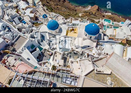 Foto panoramica aerea del pittoresco villaggio mediterraneo tradizionale di Oia, famoso in tutto il mondo, nell'isola vulcanica di Santorini, nelle Cicladi del Mar Egeo in Grecia. L'isola è famosa per il magico tramonto, l'architettura delle case imbiancate, gli hotel con vista sulla piscina e le chiese a cupola blu sul bordo ripido della scogliera. Santorini è una destinazione popolare per la luna di miele, proposte, matrimoni e coppie da tutto il mondo, ma di solito è sovraffollata di turisti asiatici come è considerato uno dei migliori luoghi romantici del mondo. Le autorità greche hanno revocato il Covi Foto Stock