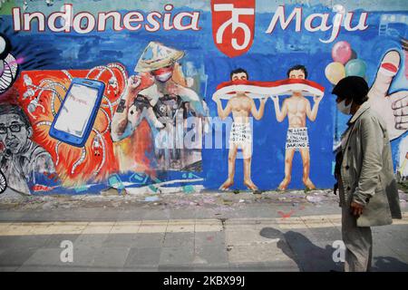 Bambang si trova di fronte al murale a tema dell'Indipendenza dipinto da lui e dagli amici sulla parete della strada accanto al suo studio di pittura di strada durante la celebrazione del 75th° giorno dell'Indipendenza dell'Indonesia a Giacarta, Indonesia, il 17 agosto 2020. Bambang Tridoyo (63), artista di pittura di strada. Ha iniziato la sua carriera dal 1975. In qualità di ammiratore del Padre fondatore dell'Indonesia, Sukarno, molte delle opere di Bambang sono ispirate da storie e figure eroiche. Non solo vendendo i suoi dipinti, accetta anche i servizi di pittura ritratto per i suoi clienti. La pandemia di Covid-19 che ha colpito l'Indonesia dalla fine di febbraio Foto Stock