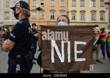 Un protettore pro-LGBT in piedi accanto ad un ufficiale di polizia ha un segno 'NO. I nazionalisti di estrema destra e gli attivisti pro-vita hanno organizzato una protesta contro l'LGBT accanto al monumento di Adam Mickiewicz nella piazza principale del mercato di Cracovia. Sul lato opposto della piazza, attivisti LGBT e antifascisti hanno organizzato una contro protesta. Il 19 agosto 2020, a Cracovia, in Polonia Voivodato minore, Polonia. (Foto di Artur Widak/NurPhoto) Foto Stock