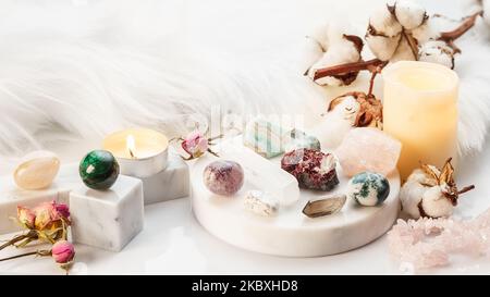 Collezione di minerali su stativo in marmo bianco con candele bruciate e fiori secchi. Pietre di guarigione per la pratica Wicca Witchcraft. Copia spazio per testo Foto Stock