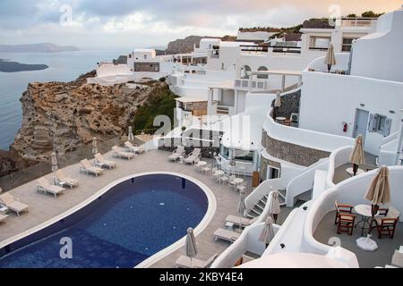 Piscina in un hotel resort a 5 stelle con sedie a sdraio e asciugamano che si affaccia su una splendida vista sulla Caldera sul mare Egeo con tradizionale architettura a terrazze greca a calce e mediterranea di case e resort. Isola di Santorini nelle Cicladi, Grecia durante una calda giornata estiva di sole. Santorini è di solito sovraffollata in quanto è famosa per il suo tramonto, che attrae soprattutto coppie da tutto il mondo per la magica vista del tramonto sul vulcano, Ma quest'anno a causa della pandemia di Coronavirus Covid-19 ci sono meno arrivi del solito, riducendo anche il reddito del PIL del conteggio Foto Stock