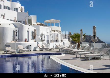 Piscina in un hotel resort a 5 stelle con sedie a sdraio e asciugamano che si affaccia su una splendida vista sulla Caldera sul mare Egeo con tradizionale architettura a terrazze greca a calce e mediterranea di case e resort. Isola di Santorini nelle Cicladi, Grecia durante una calda giornata estiva di sole. Santorini è di solito sovraffollata in quanto è famosa per il suo tramonto, che attrae soprattutto coppie da tutto il mondo per la magica vista del tramonto sul vulcano, Ma quest'anno a causa della pandemia di Coronavirus Covid-19 ci sono meno arrivi del solito, riducendo anche il reddito del PIL del conteggio Foto Stock