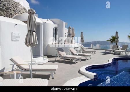 Piscina in un hotel resort a 5 stelle con sedie a sdraio e asciugamano che si affaccia su una splendida vista sulla Caldera sul mare Egeo con tradizionale architettura a terrazze greca a calce e mediterranea di case e resort. Isola di Santorini nelle Cicladi, Grecia durante una calda giornata estiva di sole. Santorini è di solito sovraffollata in quanto è famosa per il suo tramonto, che attrae soprattutto coppie da tutto il mondo per la magica vista del tramonto sul vulcano, Ma quest'anno a causa della pandemia di Coronavirus Covid-19 ci sono meno arrivi del solito, riducendo anche il reddito del PIL del conteggio Foto Stock