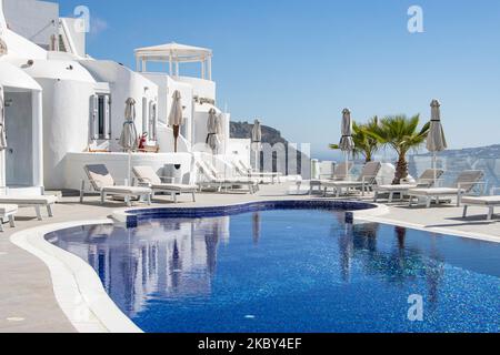 Piscina in un hotel resort a 5 stelle con sedie a sdraio e asciugamano che si affaccia su una splendida vista sulla Caldera sul mare Egeo con tradizionale architettura a terrazze greca a calce e mediterranea di case e resort. Isola di Santorini nelle Cicladi, Grecia durante una calda giornata estiva di sole. Santorini è di solito sovraffollata in quanto è famosa per il suo tramonto, che attrae soprattutto coppie da tutto il mondo per la magica vista del tramonto sul vulcano, Ma quest'anno a causa della pandemia di Coronavirus Covid-19 ci sono meno arrivi del solito, riducendo anche il reddito del PIL del conteggio Foto Stock