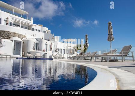 Piscina in un hotel resort a 5 stelle con sedie a sdraio e asciugamano che si affaccia su una splendida vista sulla Caldera sul mare Egeo con tradizionale architettura a terrazze greca a calce e mediterranea di case e resort. Isola di Santorini nelle Cicladi, Grecia durante una calda giornata estiva di sole. Santorini è di solito sovraffollata in quanto è famosa per il suo tramonto, che attrae soprattutto coppie da tutto il mondo per la magica vista del tramonto sul vulcano, Ma quest'anno a causa della pandemia di Coronavirus Covid-19 ci sono meno arrivi del solito, riducendo anche il reddito del PIL del conteggio Foto Stock