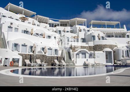 Piscina in un hotel resort a 5 stelle con sedie a sdraio e asciugamano che si affaccia su una splendida vista sulla Caldera sul mare Egeo con tradizionale architettura a terrazze greca a calce e mediterranea di case e resort. Isola di Santorini nelle Cicladi, Grecia durante una calda giornata estiva di sole. Santorini è di solito sovraffollata in quanto è famosa per il suo tramonto, che attrae soprattutto coppie da tutto il mondo per la magica vista del tramonto sul vulcano, Ma quest'anno a causa della pandemia di Coronavirus Covid-19 ci sono meno arrivi del solito, riducendo anche il reddito del PIL del conteggio Foto Stock