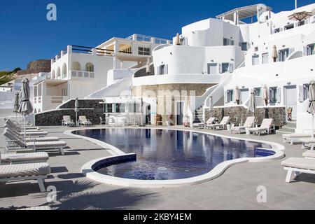 Piscina in un hotel resort a 5 stelle con sedie a sdraio e asciugamano che si affaccia su una splendida vista sulla Caldera sul mare Egeo con tradizionale architettura a terrazze greca a calce e mediterranea di case e resort. Isola di Santorini nelle Cicladi, Grecia durante una calda giornata estiva di sole. Santorini è di solito sovraffollata in quanto è famosa per il suo tramonto, che attrae soprattutto coppie da tutto il mondo per la magica vista del tramonto sul vulcano, Ma quest'anno a causa della pandemia di Coronavirus Covid-19 ci sono meno arrivi del solito, riducendo anche il reddito del PIL del conteggio Foto Stock