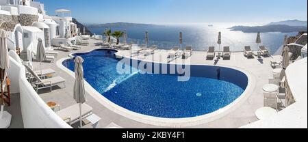 Piscina in un hotel resort a 5 stelle con sedie a sdraio e asciugamano che si affaccia su una splendida vista sulla Caldera sul mare Egeo con tradizionale architettura a terrazze greca a calce e mediterranea di case e resort. Isola di Santorini nelle Cicladi, Grecia durante una calda giornata estiva di sole. Santorini è di solito sovraffollata in quanto è famosa per il suo tramonto, che attrae soprattutto coppie da tutto il mondo per la magica vista del tramonto sul vulcano, Ma quest'anno a causa della pandemia di Coronavirus Covid-19 ci sono meno arrivi del solito, riducendo anche il reddito del PIL del conteggio Foto Stock