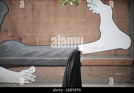 Una donna velata iraniana che indossa una maschera protettiva passa davanti a un murale nel quartiere commerciale di Teheran in mezzo alla nuova epidemia di coronavirus (COVID-19) in Iran, il 5 luglio 2020. (Foto di Morteza Nikoubazl/NurPhoto) Foto Stock