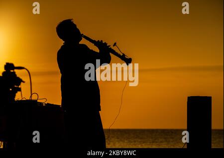 Un musicista dalla silhouette che suona sulla riva del mare contro un cielo all'alba Foto Stock