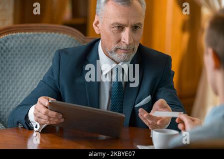 Uomo d'affari che dà il suo biglietto da visita a un uomo mentre cena nel ristorante di lusso dell'hotel Foto Stock