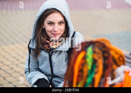 Studenti felici in abiti caldi casual parlando dopo gli studi in inverno. Emotiva giovane donna sorridente e parlando con un amico seduto al par Foto Stock