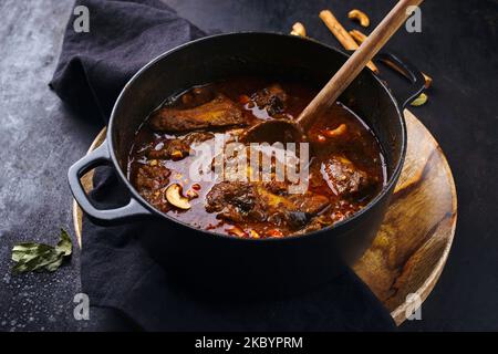 Tradizionale pollo indiano piccante Madras curry Rogan Josh con bacchette, ali di pollo e noci di anacardi tostate servito come primo piano in una pentola Foto Stock