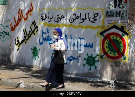 Una donna palestinese, che indossa una maschera protettiva, passa davanti a un murale raffigurante il coronavirus, mentre la malattia del coronavirus (COVID-19) restringe a Gaza City il 13 settembre 2020. (Foto di Majdi Fathi/NurPhoto) Foto Stock