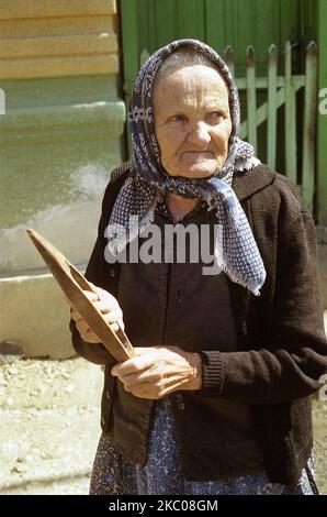 Hunedoara County, Romania, circa 2001. Donna anziana in un villaggio in possesso di una navetta telaio di legno. Foto Stock