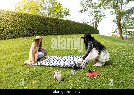 Due amici alla moda stendono una coperta sul prato di un parco Foto Stock