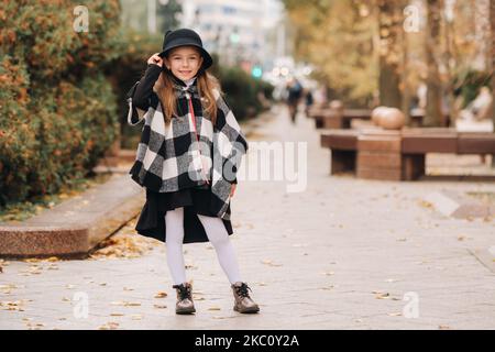 Una bambina elegante in un cappello cammina per la città autunnale Foto Stock