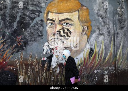 Una donna palestinese, che indossa una maschera protettiva, passa davanti a un murale raffigurante il presidente americano Donald Trump con un'impronta sul suo volto, in una strada a Gaza City il 5 ottobre 2020. (Foto di Majdi Fathi/NurPhoto) Foto Stock