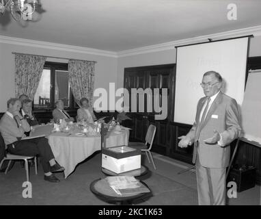 1980s, storico, formazione manageriale, in una sala conferenze dell'hotel, con lavagna bianca e lavagna luminosa, un uomo in una tuta che fa una presentazione aziendale ad alcuni dirigenti aziendali, Inghilterra, Regno Unito. Foto Stock