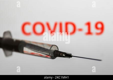 Siringa medica è visto con il segno 'COVID-19' visualizzato su uno schermo sullo sfondo in questa foto di illustrazione scattata in Polonia il 12 ottobre 2020. (Foto di Jakub Porzycki/NurPhoto) Foto Stock
