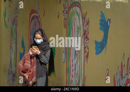 Una donna iraniana che indossa una maschera protettiva che indossa una maschera protettiva usa il suo smartphone mentre si trova di fronte a un murale nel nord di Teheran il 12 ottobre 2020. Le persone che vivono a Teheran devono indossare maschere protettive se vogliono apparire in luoghi pubblici come la nuova malattia di coronavirus (COVID-19) in rapida crescita nella capitale, secondo un ordine dei governi iraniani e dei funzionari sanitari. (Foto di Morteza Nikoubazl/NurPhoto) Foto Stock