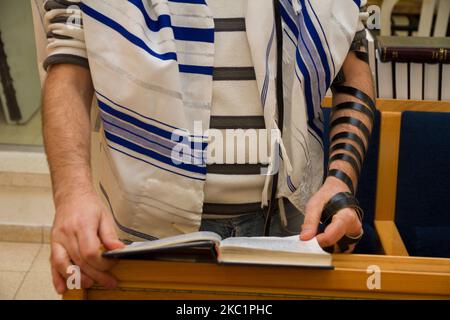 Un uomo ebreo adulto che prega con un tefillin sul braccio, tenendo un libro di bibbia, mentre legge una preghiera ad un rituale ebreo Foto Stock