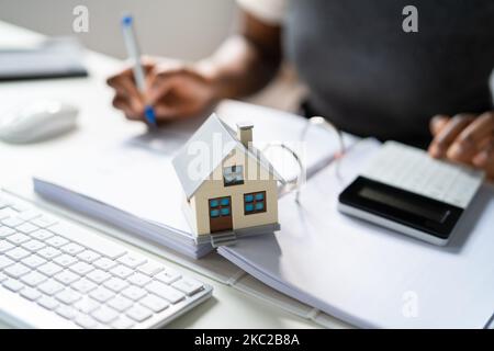 Mano della persona che fa il calcolo dell'imposta di proprietà usando il calcolatore del modello della casa Foto Stock