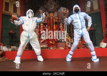 I devoti indù che indossano indumenti protettivi personali eseguono Dhunuchi, una danza tradizionale, di fronte a un idolo della dea Indù Durga durante il Durga Puja Festival presso la comunità Puja Pandal a Kolkata, in India, il 25 ottobre 2020. (Foto di Debajyoti Chakraborty/NurPhoto) Foto Stock