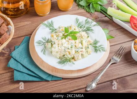 Insalata di granchio con cetrioli e uova condite con maionese in un piatto bianco su fondo di legno scuro. Foto Stock
