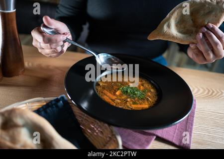 la persona mangia la zuppa di ottaggio marrone con funghi, carote, verdure, aneto e shoti Foto Stock