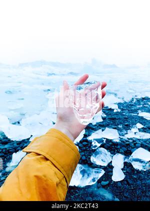 Un colpo verticale di una mano che tiene un grande pezzo di ghiaccio isolato su uno sfondo bianco Foto Stock