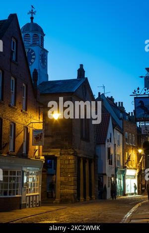 I tradizionali negozi Jet Shops lungo Church Street con il Town Hall Clock Whitby North Yorkshire England al crepuscolo Foto Stock