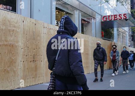 Le persone che indossano le maschere passano davanti ai negozi Guess mentre i lavoratori lo salgono in previsione di disordini legati alle elezioni presidenziali del 2 novembre 2020 a New York City. I proprietari di proprietà si stanno preparando come funzionari locali e statali avvertono della violenza in tutto il paese il giorno delle elezioni. (Foto di John Nacion/NurPhoto) Foto Stock