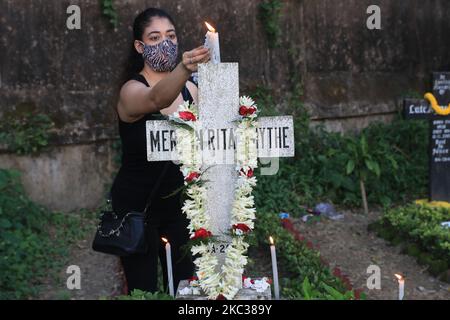 Una donna cristiana indiana che indossa maschere facciali come precauzione contro le candele di luce del coronavirus e prega accanto alla tomba di un parente durante le celebrazioni della Giornata dell'anima in un cimitero a Kolkata il 2 novembre 2020. Il giorno onora i morti mentre amici e famiglie si riuniscono nei cimiteri per decorare le tombe dei cari con candele e fiori e offrire preghiere. (Foto di Debajyoti Chakraborty/NurPhoto) Foto Stock