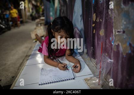 Kila, 6 anni, impara a disegnare con la luce debole di una lampada di un vicolo nel suo quartiere a Giacarta il 13 novembre 2020. Il Ministero dell'Istruzione e degli Affari culturali ha rivelato che circa 68 milioni di studenti, dai bambini in età prescolare agli studenti delle scuole superiori in Indonesia, sono stati colpiti dall'impatto della pandemia del coronavirus, che richiede loro di imparare da casa. Circa il 10 per cento dei 68 milioni di studenti indonesiani, ovvero circa 6,87 milioni, sono dei prescolatori. (Foto di Afriadi Hikmal/NurPhoto) Foto Stock