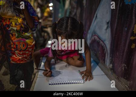 Kila, 6 anni, impara a disegnare con la luce debole di una lampada di un vicolo nel suo quartiere a Giacarta il 13 novembre 2020. Il Ministero dell'Istruzione e degli Affari culturali ha rivelato che circa 68 milioni di studenti, dai bambini in età prescolare agli studenti delle scuole superiori in Indonesia, sono stati colpiti dall'impatto della pandemia del coronavirus, che richiede loro di imparare da casa. Circa il 10 per cento dei 68 milioni di studenti indonesiani, ovvero circa 6,87 milioni, sono dei prescolatori. (Foto di Afriadi Hikmal/NurPhoto) Foto Stock