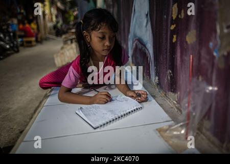 Kila, 6 anni, impara a disegnare con la luce debole di una lampada di un vicolo nel suo quartiere a Giacarta il 13 novembre 2020. Il Ministero dell'Istruzione e degli Affari culturali ha rivelato che circa 68 milioni di studenti, dai bambini in età prescolare agli studenti delle scuole superiori in Indonesia, sono stati colpiti dall'impatto della pandemia del coronavirus, che richiede loro di imparare da casa. Circa il 10 per cento dei 68 milioni di studenti indonesiani, ovvero circa 6,87 milioni, sono dei prescolatori. (Foto di Afriadi Hikmal/NurPhoto) Foto Stock