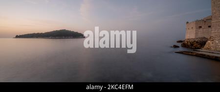 A beautiful panoramic shot of a sunrise over Lokrum island and the Walls of Dubrovnik in Croatia Foto Stock