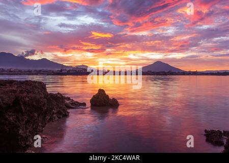 Paesaggio con rocce, spiagge, cielo rossastro al crepuscolo e piccole isole in lontananza, Foto Stock