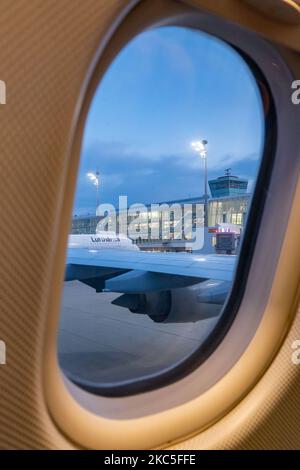 Lufthansa Airbus A350 e il Terminal dell'aeroporto come visto la mattina presto all'alba, l'ora di alba da un'altra finestra di aereo, parcheggiato alle porte dell'aeroporto internazionale di Monaco EDDM MUC. Il moderno e avanzato velivolo da A359 o A350-900 passeggeri a scocca larga è dotato della targa D-AIXO, il nome Ulm, ed è alimentato da motori a reazione 2x RR. Deutsche Lufthansa AG DLH o LH è la più grande compagnia aerea in Germania, con base hub a Francoforte, Monaco e Berlino, ex vettore di bandiera tedesco e membro fondatore del gruppo aereo della Star Alliance. Il traffico mondiale di passeggeri è diminuito durin Foto Stock