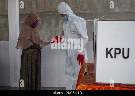 Un ufficiale indossa indumenti protettivi personali durante una votazione alla stazione di polling 08, Palupi Village, Palu City, Central Sulawesi Province, Indonesia il 9 dicembre 2020. La Provincia Centrale di Sulawesi conduce contemporaneamente l'elezione del Governatore/Vice Governatore e di sette Capi regionali a livello reggente e sindaco. Le elezioni simultanee si sono svolte anche in 270 regioni composte da 9 province, 224 regrezioni e 37 città in tutta l'Indonesia. (Foto di Basri Marzuki/NurPhoto) Foto Stock