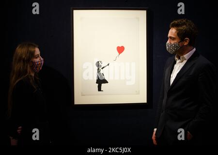 I membri del personale che indossano maschere facciali posano con 'Girl with Balloon', dell'artista britannico Banksy, valutato a 120.000-180.000GBP, durante una chiamata fotografica per la prossima vendita di stampe e multipli presso la casa d'asta di Bonhams a Londra, Inghilterra, il 10 dicembre 2020. La vendita si svolge martedì 15 dicembre. (Foto di David Cliff/NurPhoto) Foto Stock