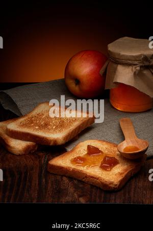 Fette croccanti di pane tostato con marmellata di mele su tavolo di legno scuro e caldo sfondo rustico Foto Stock