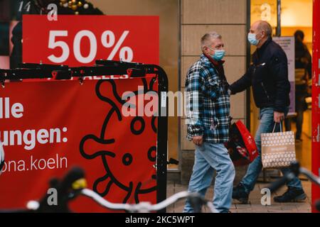 Due amanti dello shopping passeranno il cartello di vendita delle offerte e il cartello di Coronavirus nel centro della città, a Colonia, in Germania, il 14 dicembre 2020, in mezzo alla pandemia del Covid-19. (Foto di Ying Tang/NurPhoto) Foto Stock