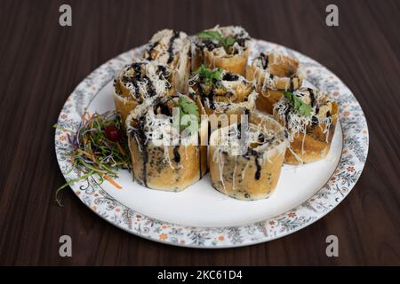 Un piatto bianco pieno di delizioso DOSA indiano avvolge su un tavolo di legno Foto Stock