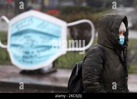 Una donna che indossa una maschera protettiva in mezzo all'epidemia di coronavirus COVID-19 cammina accanto a un oggetto d'arte della più grande maschera medica in Ucraina durante un evento in piazza Kontraktova nel centro di Kyiv, Ucraina il 28 dicembre 2020. L'evento intitolato "Cover Yourself with a mask, not Inside Yourself" fa parte della campagna sociale finalizzata a richiamare l'attenzione sui problemi di salute mentale durante la pandemia di coronavirus del Covid-19, come hanno riferito i media locali. Le lettere della mascherina gradiscono: 'Se soltanto non ottenere ammalato ', 'sono impaurito per i miei genitori ', 'realmente perderò il mio lavoro?', 'quando vedrò i miei nipoti?', ' Foto Stock