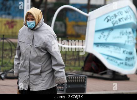 Una donna anziana che indossa una maschera protettiva in mezzo all'epidemia di coronavirus COVID-19 cammina accanto a un oggetto d'arte della più grande maschera medica in Ucraina durante un evento in piazza Kontraktova nel centro di Kyiv, Ucraina il 28 dicembre 2020. L'evento intitolato "Cover Yourself with a mask, not Inside Yourself" fa parte della campagna sociale finalizzata a richiamare l'attenzione sui problemi di salute mentale durante la pandemia di coronavirus del Covid-19, come hanno riferito i media locali. Le lettere della mascherina gradiscono: 'Se soltanto non ottenere ammalato ', 'sono impaurito per i miei genitori ', 'realmente perderò il mio lavoro?', 'quando vedrò il mio grandchil Foto Stock