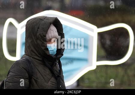 Una donna che indossa una maschera protettiva in mezzo all'epidemia di coronavirus COVID-19 cammina accanto a un oggetto d'arte della più grande maschera medica in Ucraina durante un evento in piazza Kontraktova nel centro di Kyiv, Ucraina il 28 dicembre 2020. L'evento intitolato "Cover Yourself with a mask, not Inside Yourself" fa parte della campagna sociale finalizzata a richiamare l'attenzione sui problemi di salute mentale durante la pandemia di coronavirus del Covid-19, come hanno riferito i media locali. Le lettere della mascherina gradiscono: 'Se soltanto non ottenere ammalato ', 'sono impaurito per i miei genitori ', 'realmente perderò il mio lavoro?', 'quando vedrò i miei nipoti?', ' Foto Stock