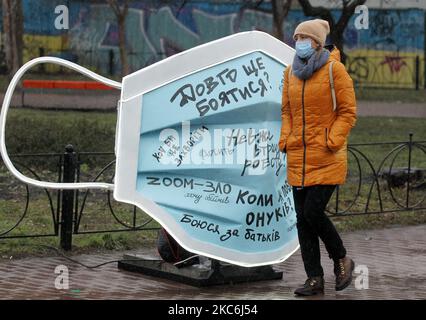 Una donna che indossa una maschera protettiva in mezzo all'epidemia di coronavirus COVID-19 cammina accanto a un oggetto d'arte della più grande maschera medica in Ucraina durante un evento in piazza Kontraktova nel centro di Kyiv, Ucraina il 28 dicembre 2020. L'evento intitolato "Cover Yourself with a mask, not Inside Yourself" fa parte della campagna sociale finalizzata a richiamare l'attenzione sui problemi di salute mentale durante la pandemia di coronavirus del Covid-19, come hanno riferito i media locali. Le lettere della mascherina gradiscono: 'Se soltanto non ottenere ammalato ', 'sono impaurito per i miei genitori ', 'realmente perderò il mio lavoro?', 'quando vedrò i miei nipoti?', ' Foto Stock